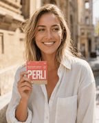Person smiling on a sunlit street holding a Perli Cinna Mint pack