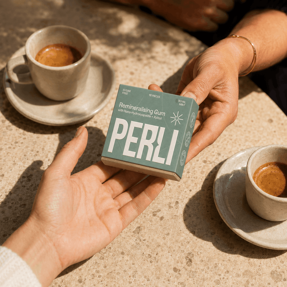 Hand passing a Perli Royal Mint pack to another person across a cafe table